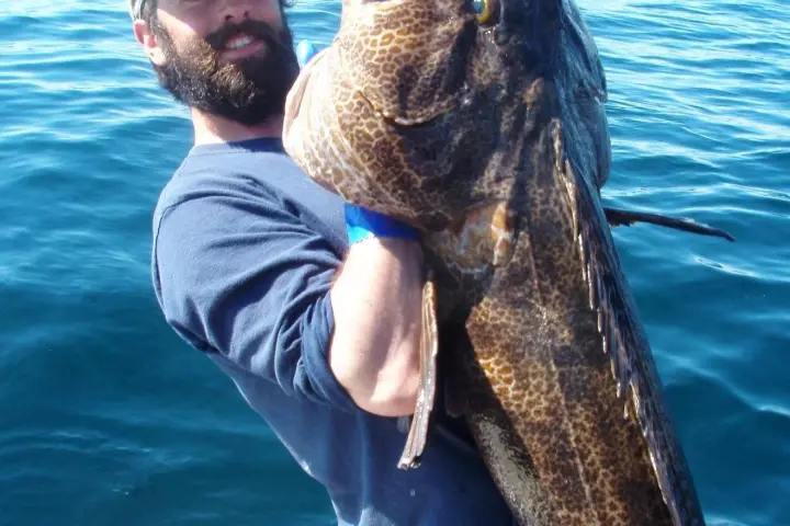 a man holding a fish on a boat in a body of water